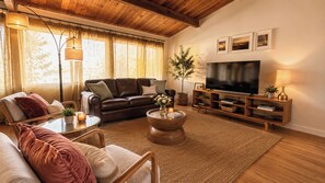 Ein gemütliches Wohnzimmer mit Ledersofa, runder Couchtisch, Fernseher und Bücherregal.