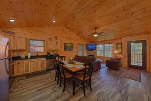 A cabin interior with a wooden dining table, chairs, a sofa, a television, and a fireplace. - Lazy Bear Lodge | Hot Tub, Game Room, Resort Pool + Free Attraction Tickets (Sevierville)