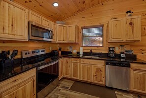 A kitchen with wooden cabinets, a microwave, stove, oven, and a dishwasher. - Lazy Bear Lodge | Hot Tub, Game Room, Resort Pool + Free Attraction Tickets (Sevierville)