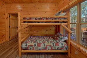 A bunk bed with a quilted bedspread and pillows, wooden walls, and a window with a view of trees. - Lazy Bear Lodge | Hot Tub, Game Room, Resort Pool + Free Attraction Tickets (Sevierville)