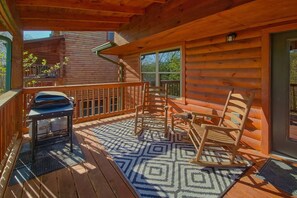 A wooden deck with a grill, outdoor seating, and a patterned rug. - Lazy Bear Lodge | Hot Tub, Game Room, Resort Pool + Free Attraction Tickets (Sevierville)