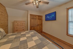 A bedroom with a bed, a dresser, a wooden door, a ceiling fan, a wall-mounted TV, and a window with blinds. - Breathtaker Cabin Rental (Pigeon Forge)