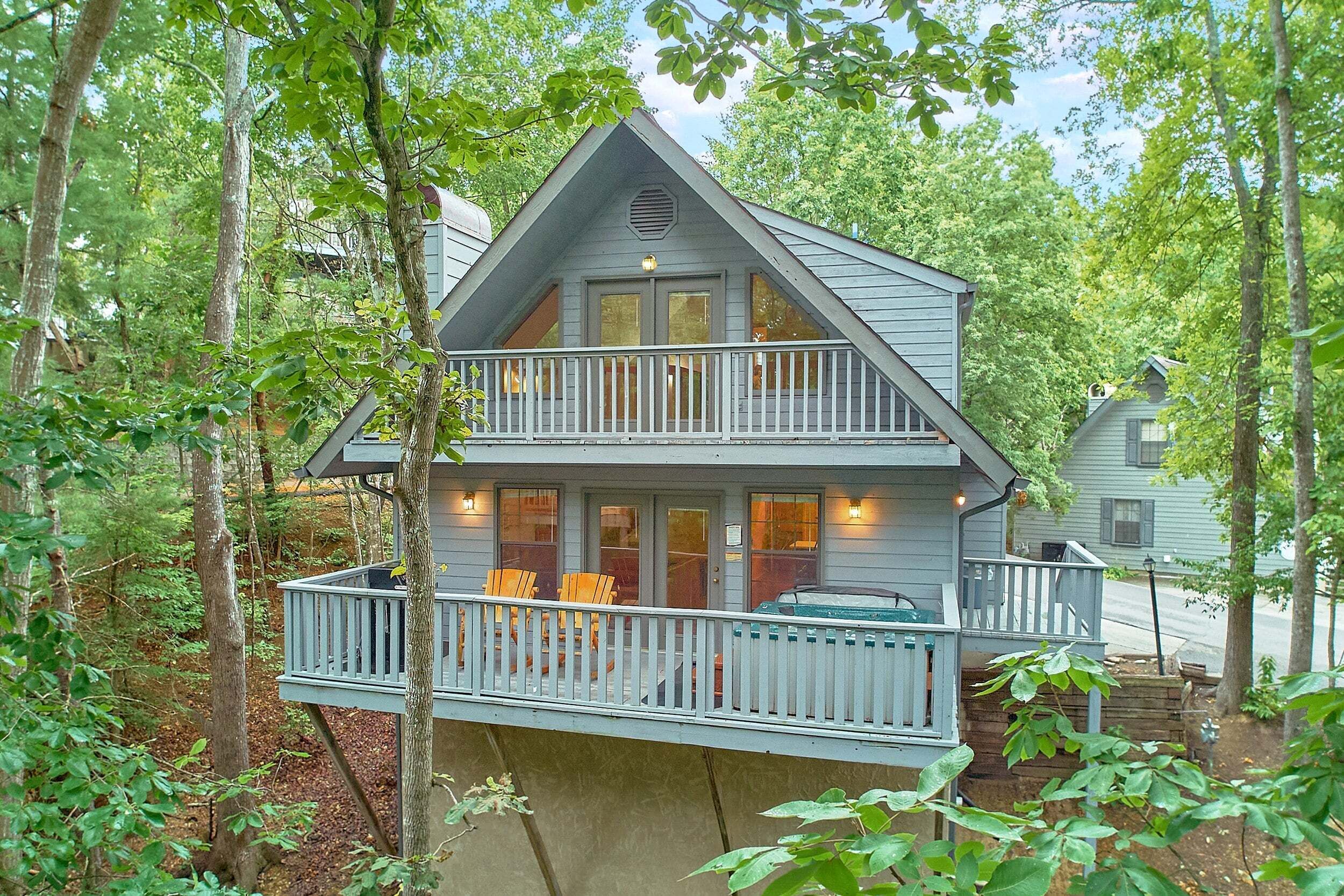 A two-story cabin with a balcony, surrounded by trees.