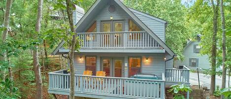 A two-story cabin with a balcony, surrounded by trees.