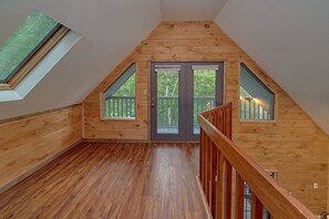 A wooden interior with a sloped ceiling, a wooden staircase, and a door leading to an outdoor area. - Breathtaker Cabin Rental (Pigeon Forge)