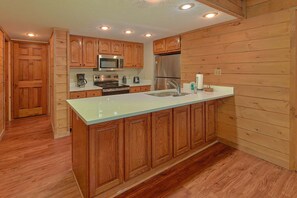 A kitchen with wooden cabinetry, a stainless steel refrigerator, a microwave, and a sink. - Breathtaker Cabin Rental (Pigeon Forge)
