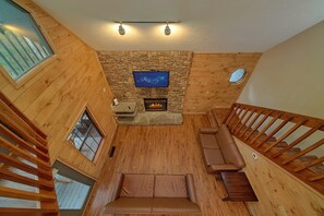 A high-ceilinged room with a stone fireplace, a flat-screen TV mounted on the wall, and a wooden staircase. - Breathtaker Cabin Rental (Pigeon Forge)