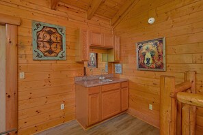 A wooden cabin interior with a kitchen area, wooden walls, and two framed artworks. - Above the Rest | Game Room | Hot Tub | Fireplace (Sevierville)