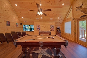 A pool table with surrounding chairs, a ceiling fan, and a large window with blinds. - Amazing Mountain Cabin Rental (Sevierville)