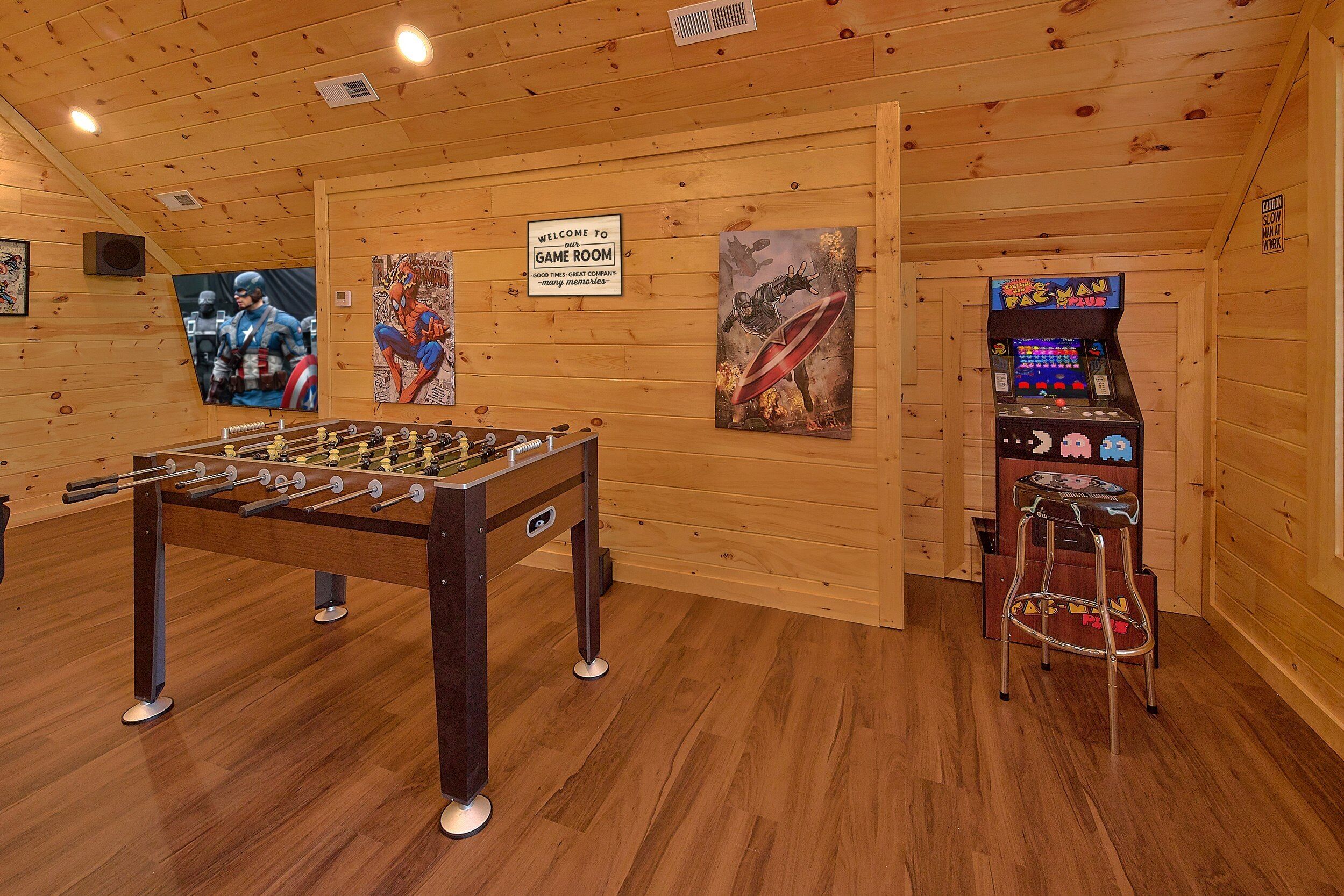 Um quarto com paredes de madeira, uma mesa de futebol de mesa e um fliperama do Pac-Man.