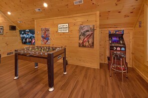 A room with wooden walls, a foosball table, and a Pac-Man arcade machine. - Amazing Mountain Cabin Rental (Sevierville)