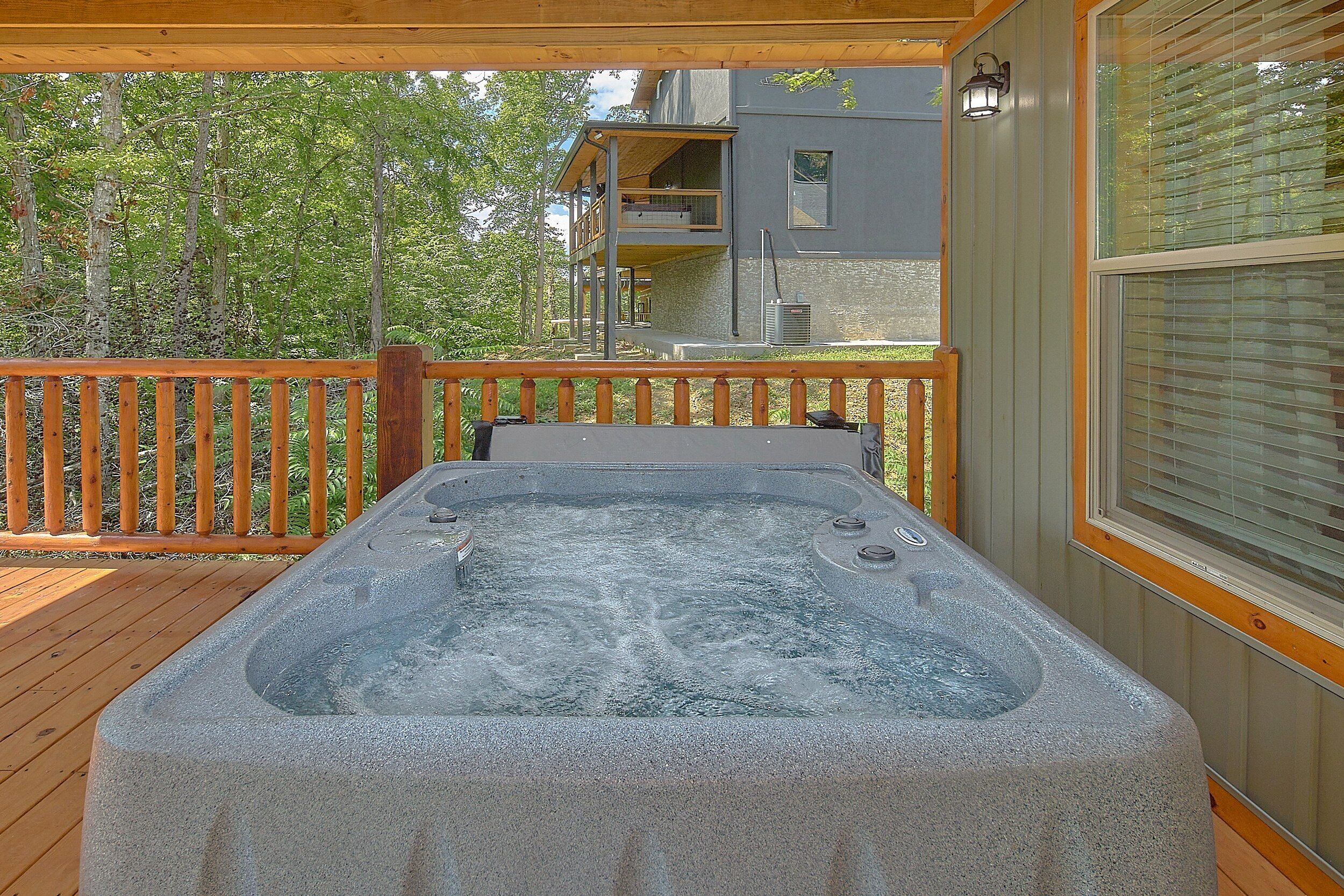 Un bain à remous sur une terrasse en bois, avec vue sur un immeuble et des arbres.