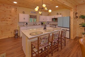 A kitchen with wooden walls, a central island with bar stools, a double refrigerator, and a chandelier. - Amazing Mountain Cabin Rental (Sevierville)