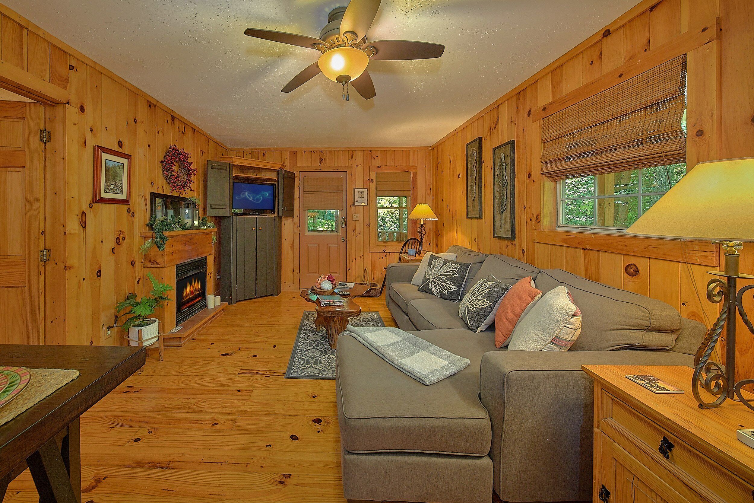 A cozy cabin interior with a fireplace, wooden walls, a sofa, and a television.