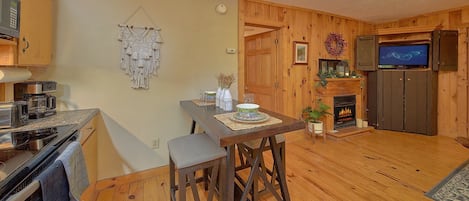 Une cuisine chaleureuse aux murs en bois, avec une table à manger et des tabourets, une machine à café et un téléviseur.