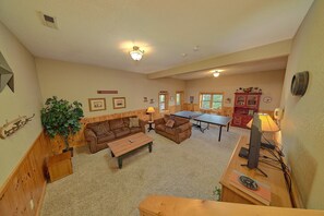 A cozy living room with a sofa, coffee table, and a ping pong table. - Timberwolf | Smoky Mtn Views, Hot Tub, Game Room, King Suites, Fireplace + Free Attraction Tickets (Wears Valley)