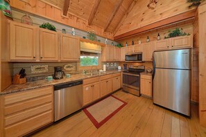 A kitchen with wooden cabinets, a stainless steel refrigerator, a microwave, and a dishwasher. - Timberwolf | Smoky Mtn Views, Hot Tub, Game Room, King Suites, Fireplace + Free Attraction Tickets (Wears Valley)