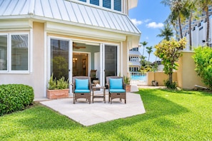A house with a covered patio, two wicker chairs with cushions, a small table, and a potted plant.