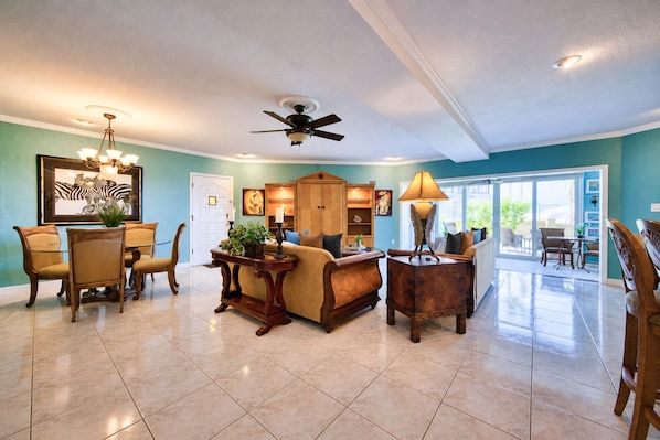 A spacious living room with a dining area, a ceiling fan, and a view to the outside.