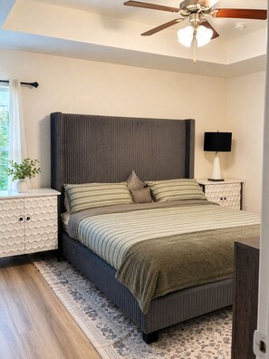 A bedroom with a large bed, a ceiling fan, a nightstand with a lamp, and a window with curtains. - 
The Perfect Getaway: 2BR Luxury Retreat (Harker Heights)