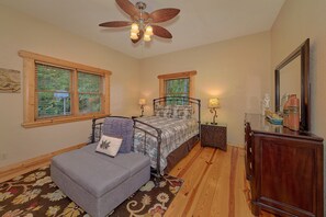 A bedroom with two beds, a ceiling fan, a nightstand with a lamp, a dresser, and a mirror.
