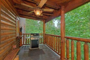 A wooden deck with a grill, a ceiling fan, and a view of a forest.