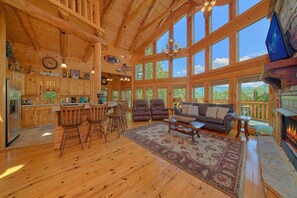 A spacious cabin interior with a large open living area, a kitchen with wooden cabinets, and a fireplace.