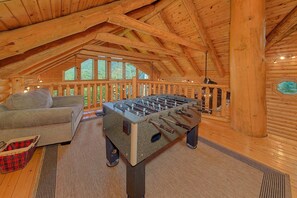 A cozy room with a foosball table, a sofa, and a window overlooking greenery.