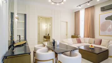 A modern living room with a sofa, coffee table, and chairs. There is a dining area with a table and chairs. The room has a large window with curtains.