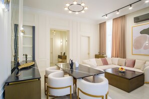 A modern living room with a sofa, coffee table, and chairs. There is a dining area with a table and chairs. The room has a large window with curtains. - BB Signature Collection (Tbilisi)