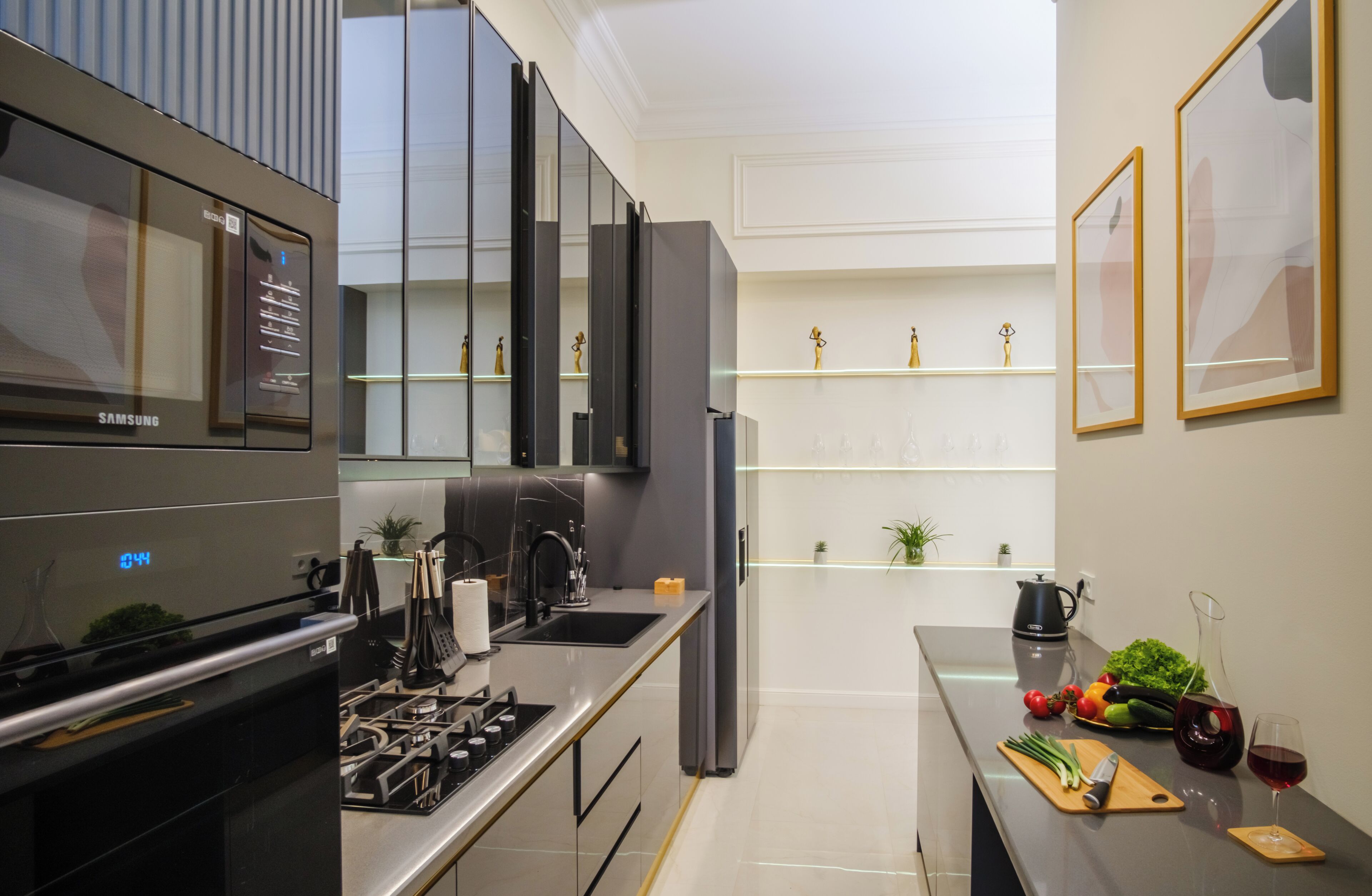 A modern kitchen with a built-in oven, a stainless steel sink, and a countertop with a kettle and a wine glass.
