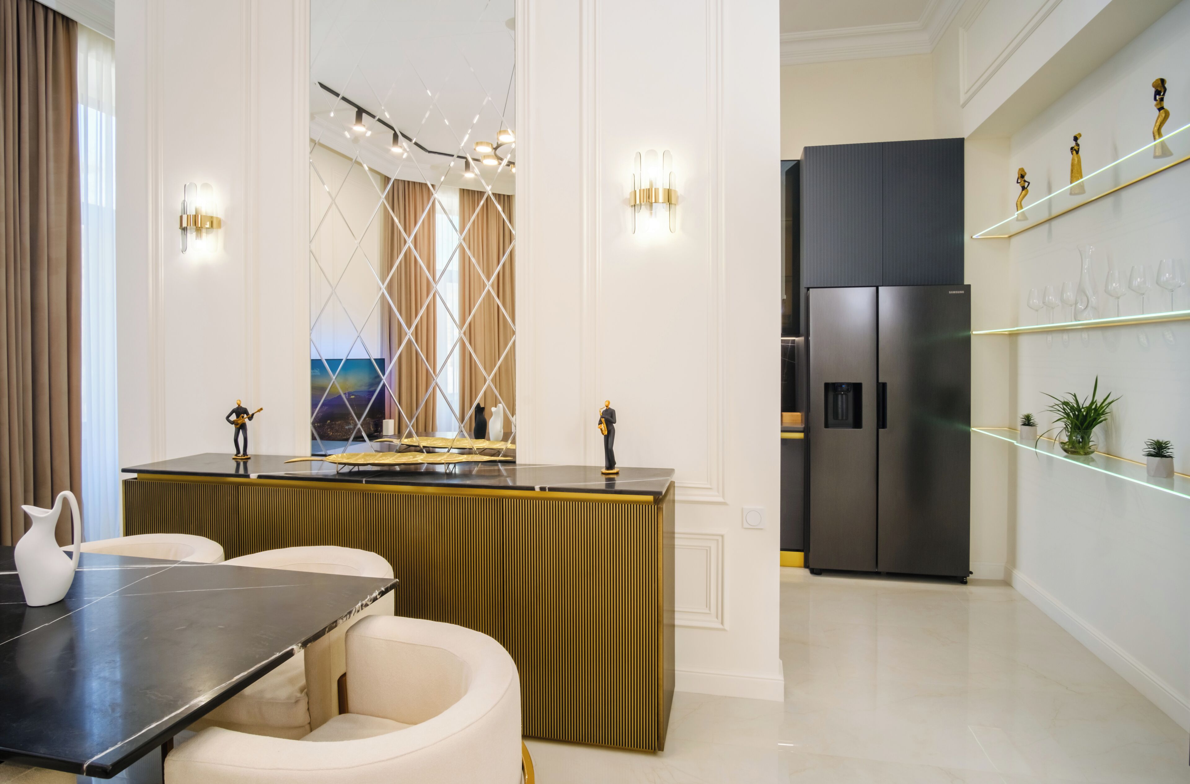 Cozinha moderna com geladeira preta, área de jantar com mesa preta e cadeiras brancas, e uma parede decorativa com prateleiras.