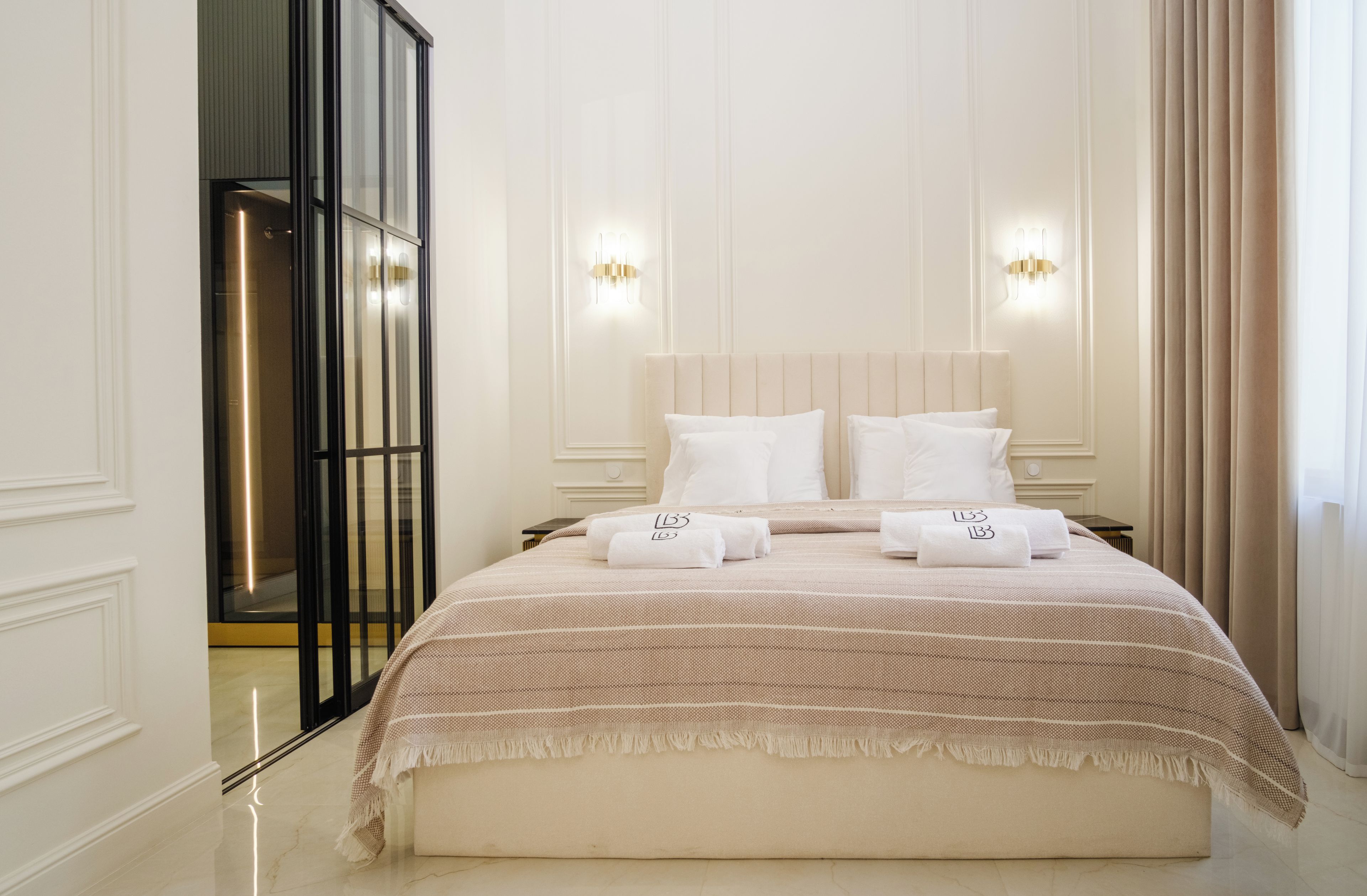 A hotel room with a large bed, two wall-mounted lights, a mirror, and a door with a glass panel.