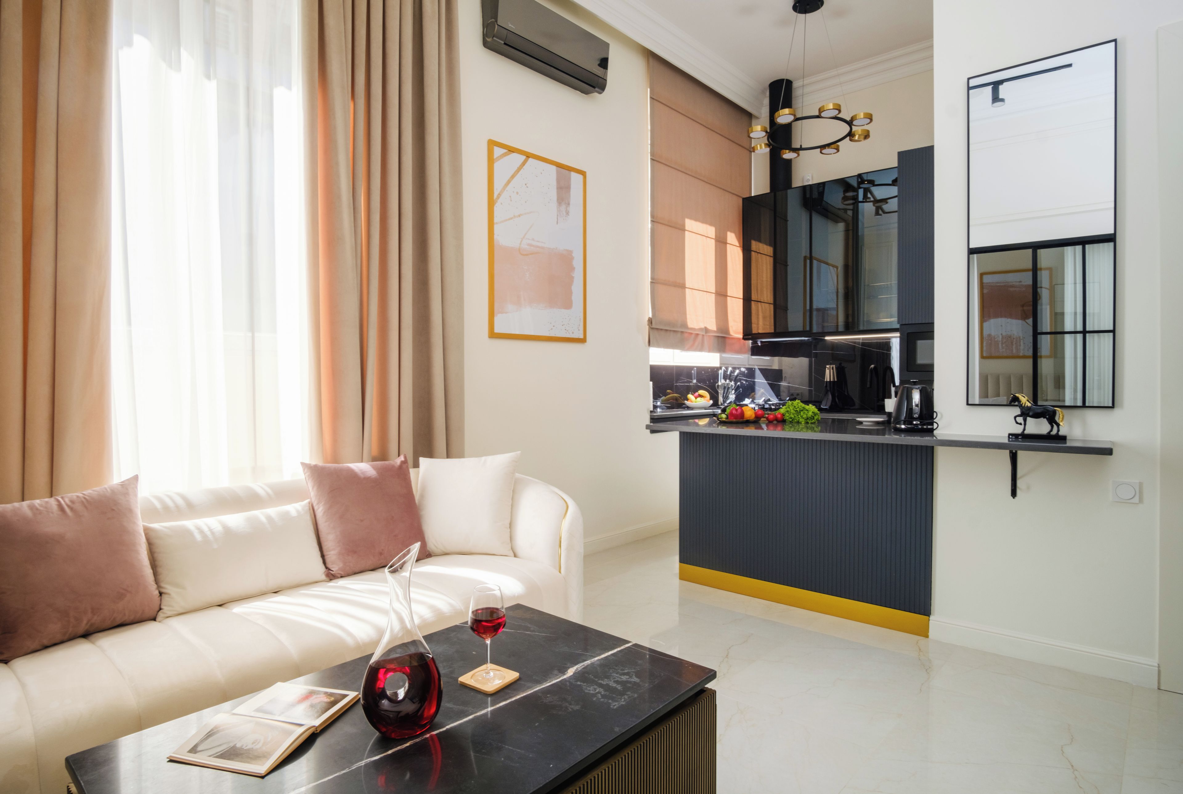 A modern living room with a sofa, a coffee table with a wine glass and book, and a kitchen area with a counter and appliances.
