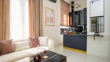 A modern living room with a sofa, a coffee table with a wine glass and book, and a kitchen area with a counter and appliances.