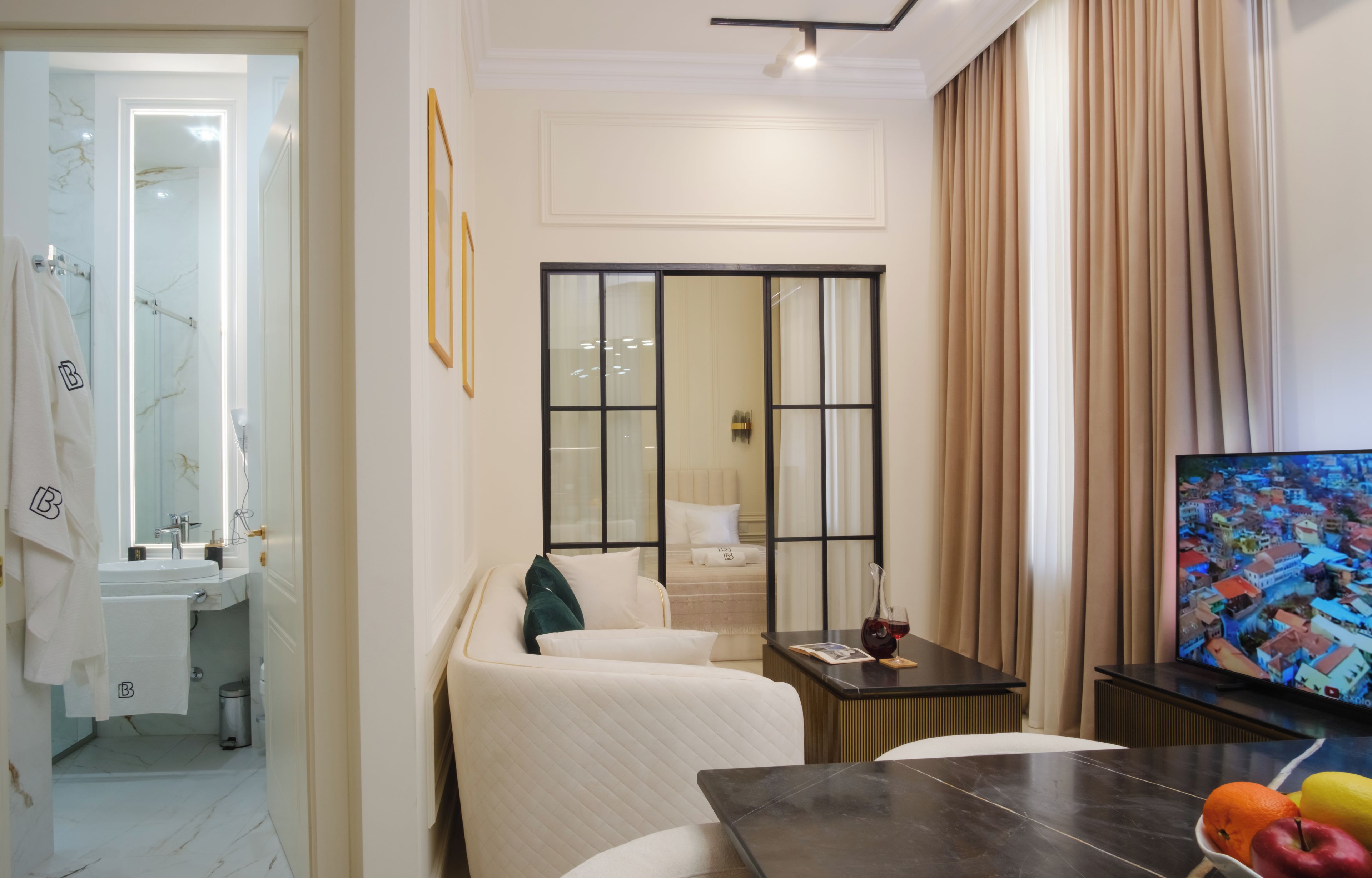 A modern hotel room with a bed, a TV, a dining table, and a view of a cityscape.