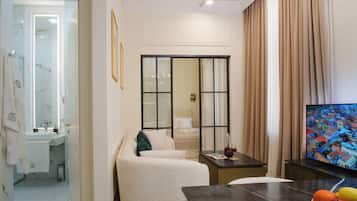 A modern hotel room with a bed, a TV, a dining table, and a view of a cityscape.