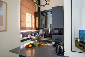 A modern kitchen with a built-in microwave, stove, and sink. There is a fruit bowl with various fruits and vegetables on the counter. - BB Signature Collection (Tbilisi)
