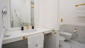 Un bany amb un lavabo blanc, un mirall gran, un aixeta daurada i un vàter.