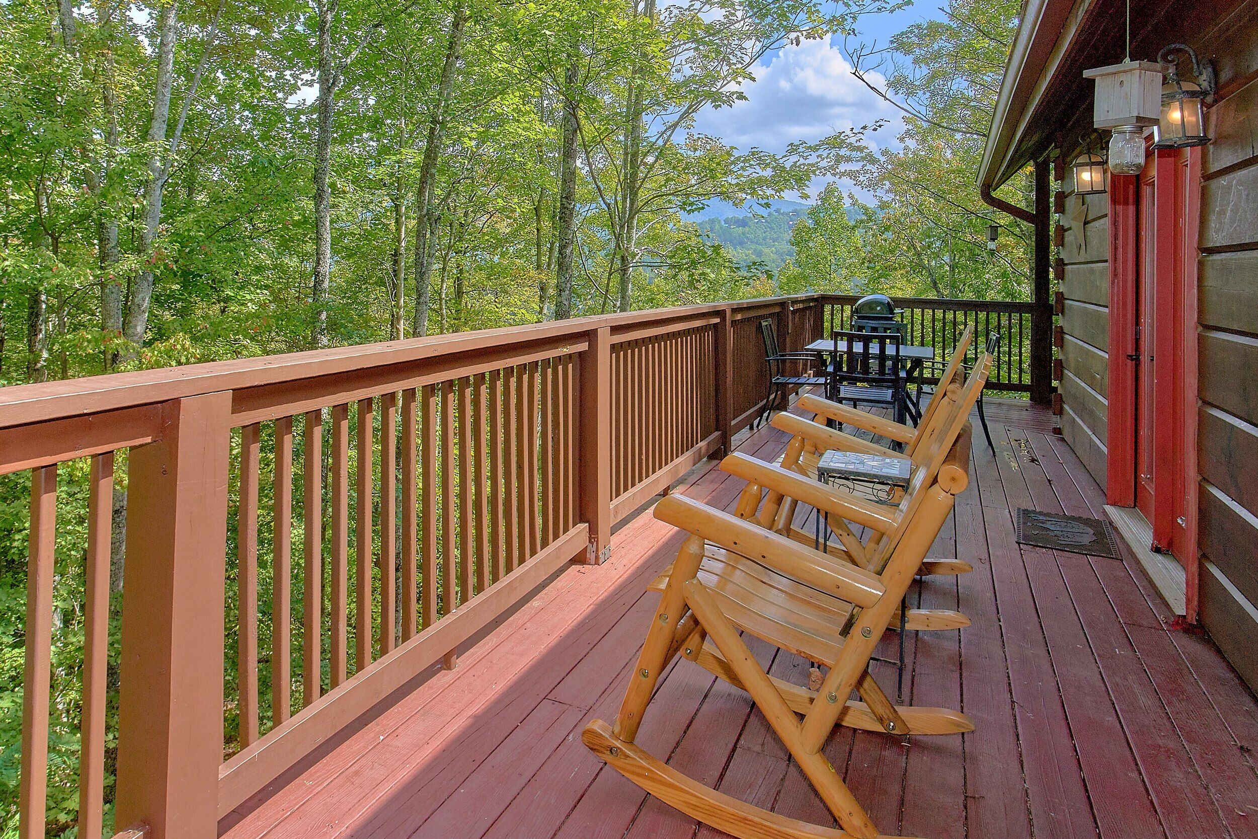 A wooden deck with a railing, a rocking chair, and a table with chairs.