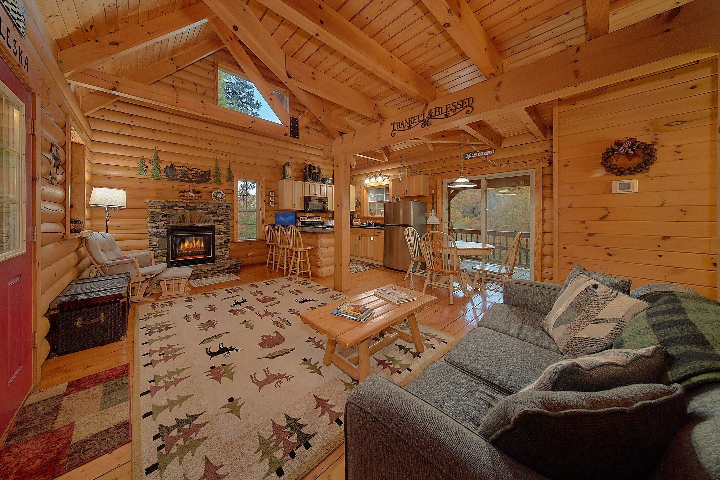 A log cabin interior with a fireplace, wooden furniture, and a view of the outdoors.