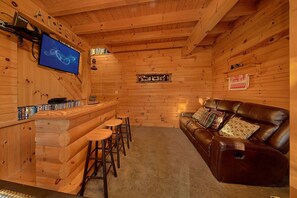 Ein gemütliches Blockhaus-Interieur mit einer Holzbar, einem Ledersofa und einem wandmontierten Fernseher.