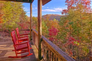 A wooden deck with red chairs and a view of autumn foliage. - Aleska 1 Bedroom Cabin Rental (Wears Valley)