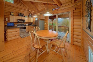 Ein Ferienhaus-Interieur mit einem Holztisch, Stühlen, einer Küche mit Geräten und Blick durch eine Glastür.