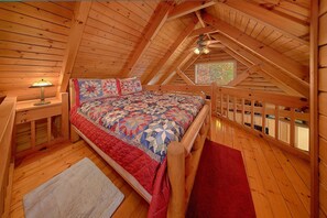 Ein Schlafzimmer im Dachgeschoss mit Holzboden, einem Bett, einem Nachttisch, einer Lampe und einem Fenster mit Aussicht.