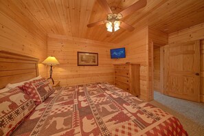 A wooden cabin room with a bed, a lamp, a framed picture, a television, and a door. - Rocky Top Joy | Mtn Views, Game Room, Resort Pool, Fireplace + Free Attraction Tickets (Townsend)