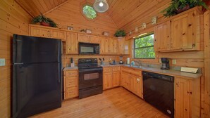 Une cuisine rustique aménagée dans une cabane en bois, équipée d’un réfrigérateur, d’une cuisinière, d’un four à micro-ondes, d’un évier et d’un lave-vaisselle.
