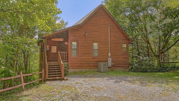 Une cabane en bois avec un escalier menant à l’entrée, entourée d’arbres.