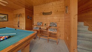 L’intérieur d’un chalet en bois comprend une table de billard, deux chaises, une petite table et un escalier.