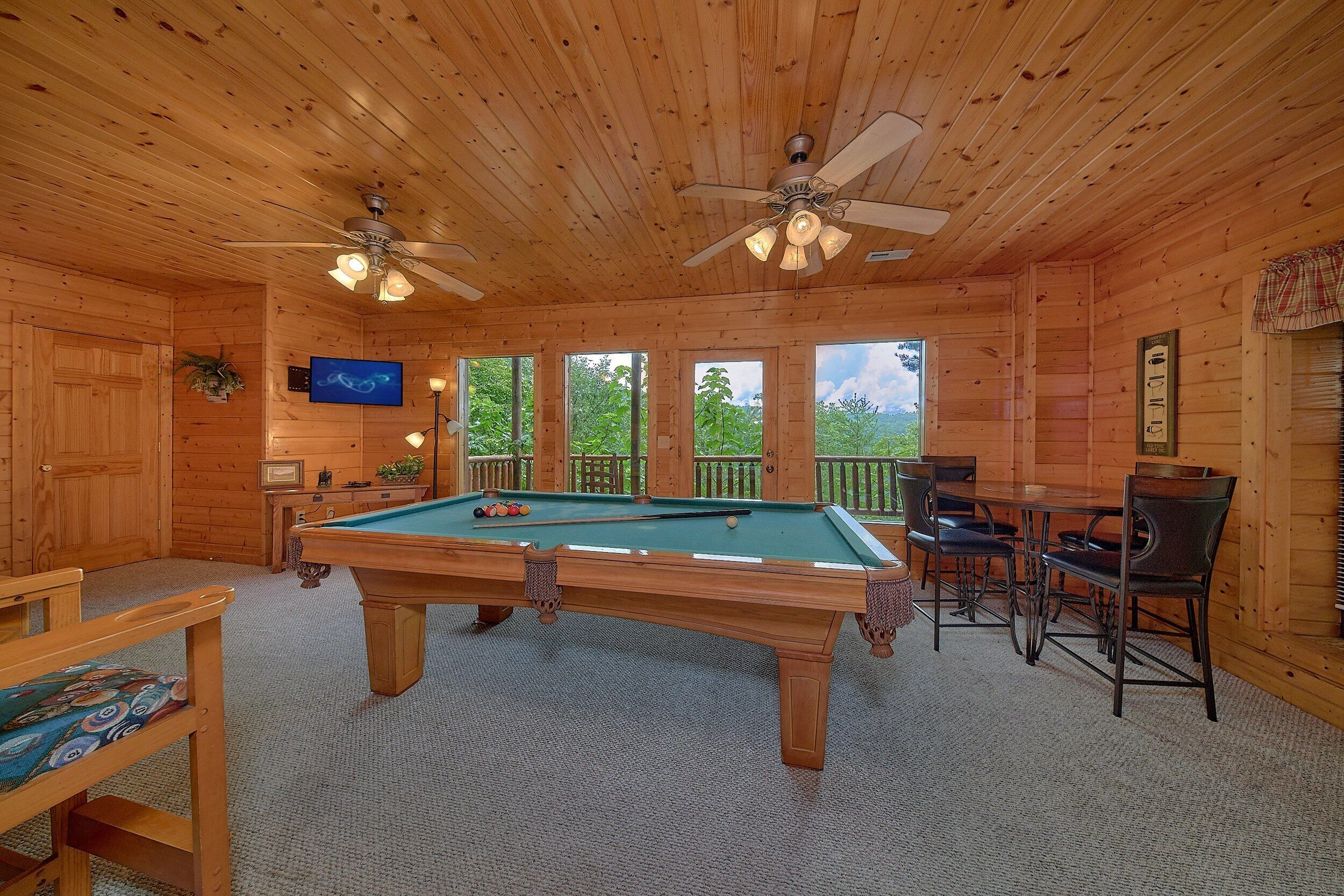 Un intérieur en bois avec une table de billard, des ventilateurs de plafond et une vue sur la verdure environnante.